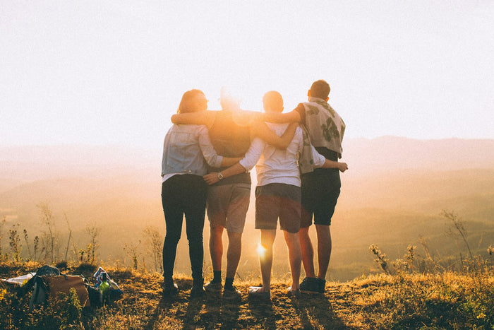 Gruppe von Menschen, die sich bei Sonnenuntergang umarmen, als Collage-Bild mit der Bedeutung von Verbundenheit, Beziehungen und Unterstützung